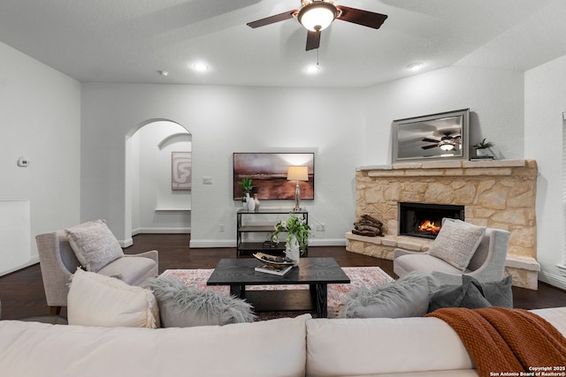 living room with dark wood-type flooring, ceiling fan, and a stone fireplace