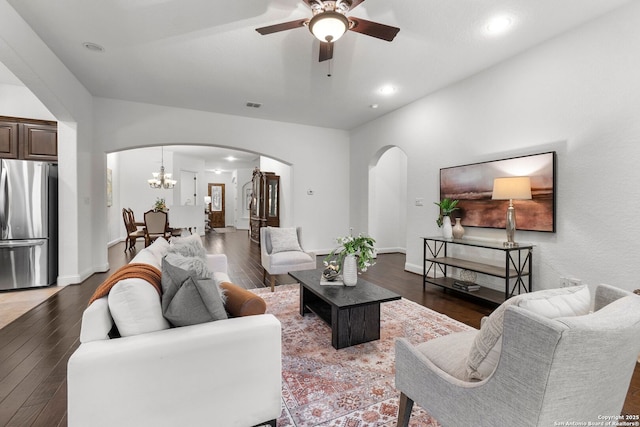 living room with ceiling fan with notable chandelier and dark hardwood / wood-style flooring