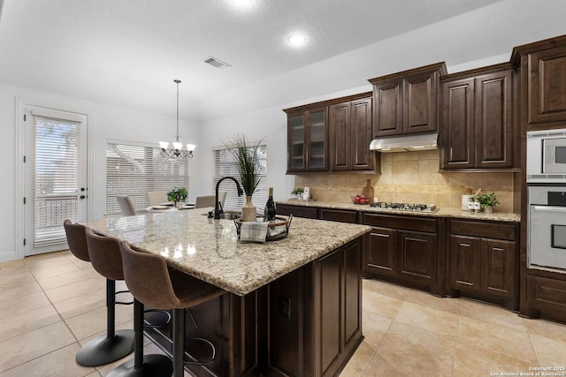 kitchen featuring pendant lighting, appliances with stainless steel finishes, an island with sink, and dark brown cabinets