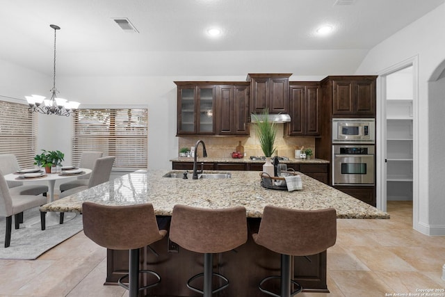 kitchen with sink, a kitchen island with sink, dark brown cabinets, stainless steel appliances, and tasteful backsplash