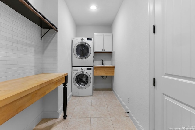 clothes washing area with sink, stacked washer / drying machine, light tile patterned floors, and cabinets