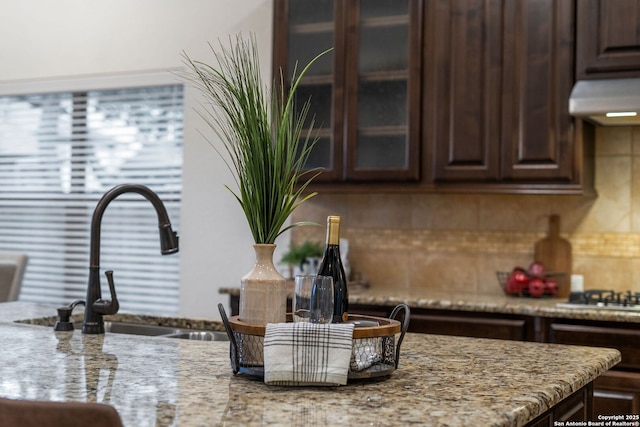 kitchen featuring tasteful backsplash, light stone countertops, sink, and dark brown cabinets