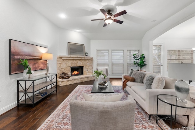 living room with dark hardwood / wood-style flooring, a stone fireplace, vaulted ceiling, and ceiling fan