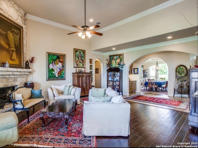 living room featuring crown molding, a stone fireplace, ceiling fan, and dark hardwood / wood-style flooring