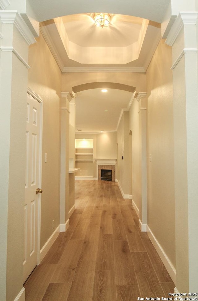 corridor featuring a tray ceiling, hardwood / wood-style flooring, ornamental molding, and decorative columns