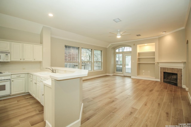 kitchen with sink, white cabinetry, kitchen peninsula, white appliances, and light hardwood / wood-style floors