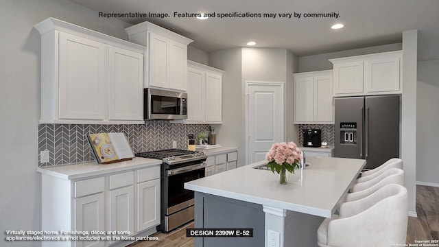 kitchen with a breakfast bar, a center island with sink, light wood-type flooring, stainless steel appliances, and white cabinets