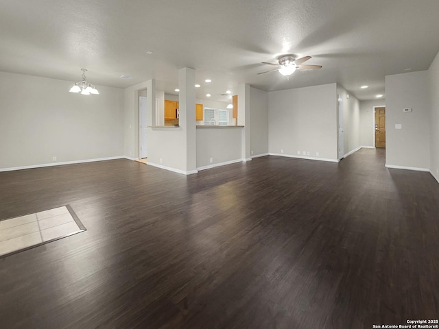 unfurnished living room featuring ceiling fan with notable chandelier, dark wood-type flooring, and a textured ceiling