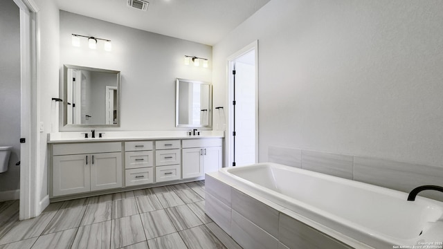 bathroom with vanity, tiled bath, and toilet