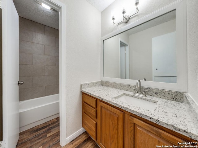 bathroom with tiled shower / bath combo, vanity, hardwood / wood-style floors, and a textured ceiling