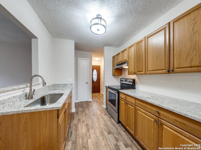 kitchen with sink, stainless steel electric range, light hardwood / wood-style flooring, light stone counters, and decorative backsplash