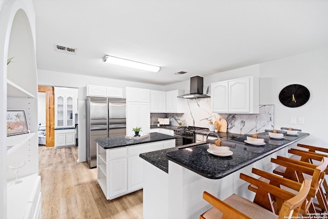 kitchen featuring white cabinetry, appliances with stainless steel finishes, wall chimney exhaust hood, and a center island