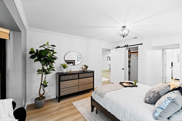 bedroom featuring a spacious closet, ornamental molding, light hardwood / wood-style floors, and a barn door