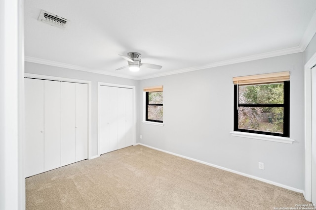 unfurnished bedroom with multiple windows, crown molding, light carpet, and multiple closets