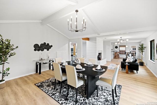 dining room featuring vaulted ceiling with beams, a fireplace, light hardwood / wood-style floors, and a chandelier