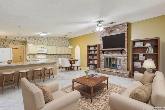 living room featuring a brick fireplace, a textured ceiling, ceiling fan, and light tile patterned flooring