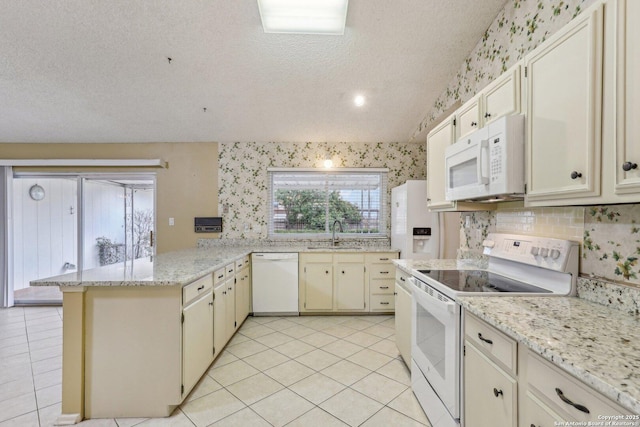 kitchen featuring sink, light stone counters, kitchen peninsula, white appliances, and cream cabinets