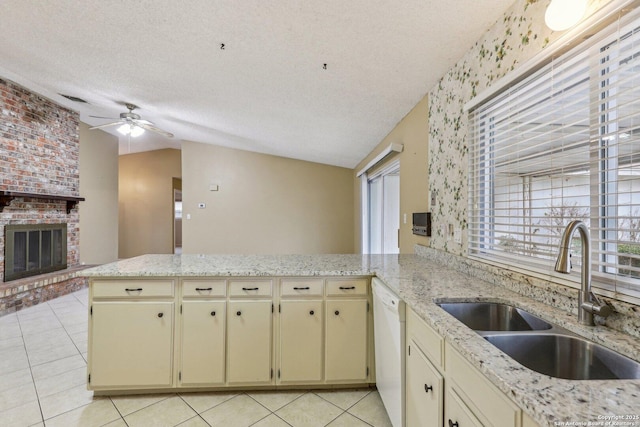 kitchen with sink, white dishwasher, kitchen peninsula, a brick fireplace, and cream cabinetry