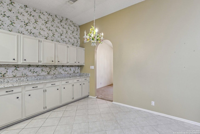 kitchen featuring light tile patterned flooring, an inviting chandelier, hanging light fixtures, light stone countertops, and white cabinets