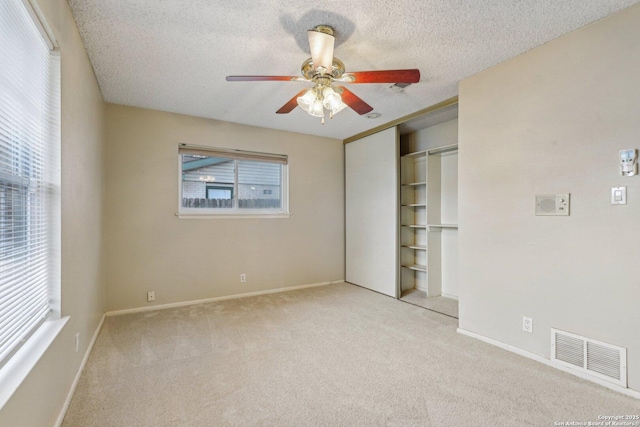 unfurnished bedroom with ceiling fan, light colored carpet, a textured ceiling, and a closet