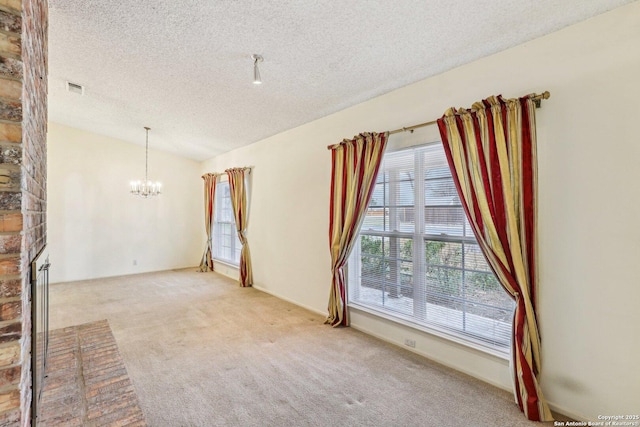 carpeted empty room with a brick fireplace, a chandelier, vaulted ceiling, and a textured ceiling