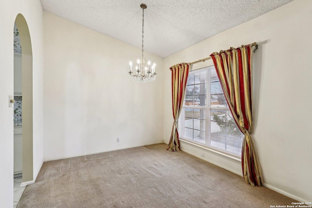 carpeted spare room featuring an inviting chandelier, vaulted ceiling, and a textured ceiling