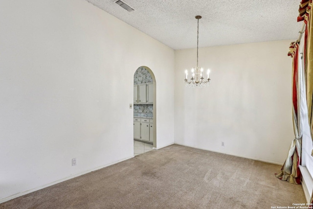 carpeted empty room with an inviting chandelier and a textured ceiling