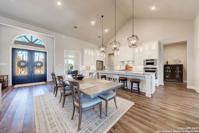 dining area with light hardwood / wood-style flooring, high vaulted ceiling, and french doors