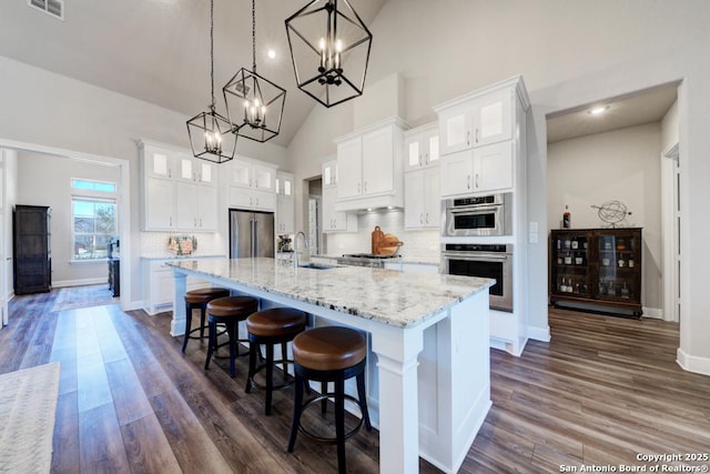 kitchen with white cabinetry, decorative light fixtures, a large island with sink, stainless steel appliances, and decorative backsplash