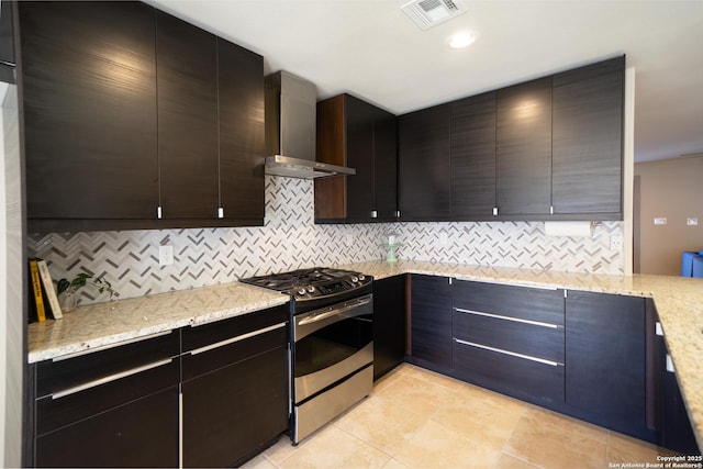 kitchen with light stone counters, wall chimney range hood, tasteful backsplash, and stainless steel range with gas stovetop