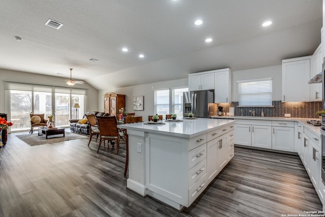 kitchen featuring visible vents, lofted ceiling, a kitchen island, open floor plan, and stainless steel refrigerator with ice dispenser