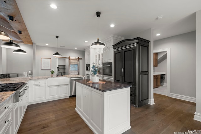 kitchen with sink, white cabinetry, stainless steel appliances, decorative light fixtures, and a barn door