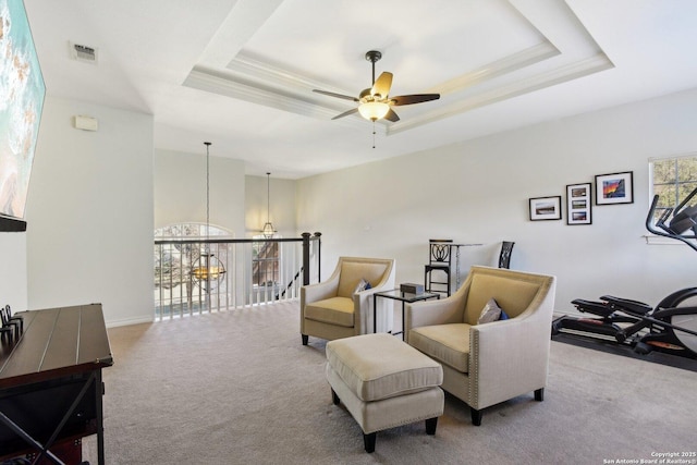 living area with ceiling fan, a tray ceiling, and light carpet