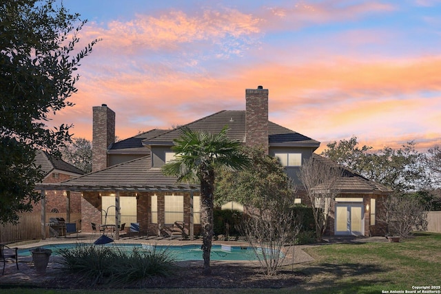 back house at dusk with french doors, a fenced in pool, and a lawn