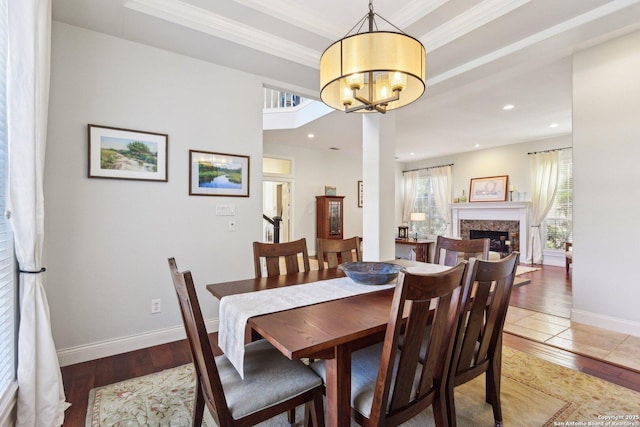 dining space with hardwood / wood-style floors, a notable chandelier, a high end fireplace, a raised ceiling, and crown molding