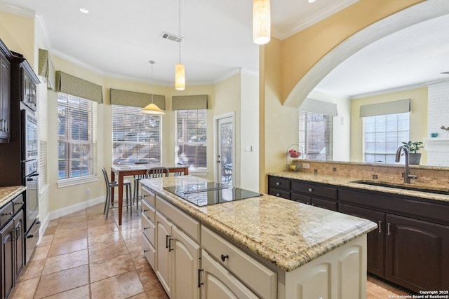 kitchen with a kitchen island, dark brown cabinets, sink, and light stone counters