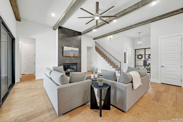 living room featuring beam ceiling, ceiling fan with notable chandelier, a tile fireplace, and light hardwood / wood-style flooring