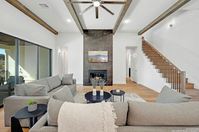 living room with ceiling fan, beam ceiling, a tiled fireplace, and light hardwood / wood-style floors