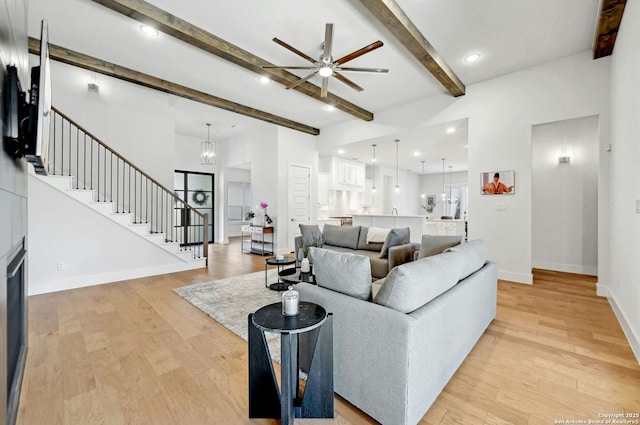 living room featuring beam ceiling, ceiling fan with notable chandelier, and light hardwood / wood-style floors