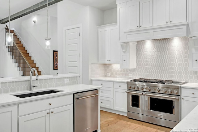 kitchen with decorative light fixtures, white cabinetry, sink, stainless steel appliances, and light stone countertops