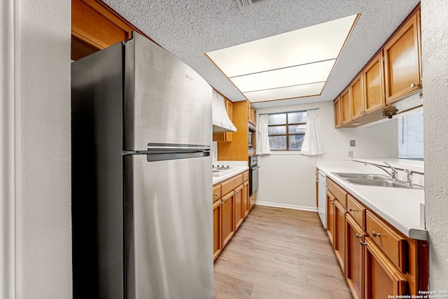 kitchen featuring sink, light hardwood / wood-style flooring, a textured ceiling, appliances with stainless steel finishes, and range hood