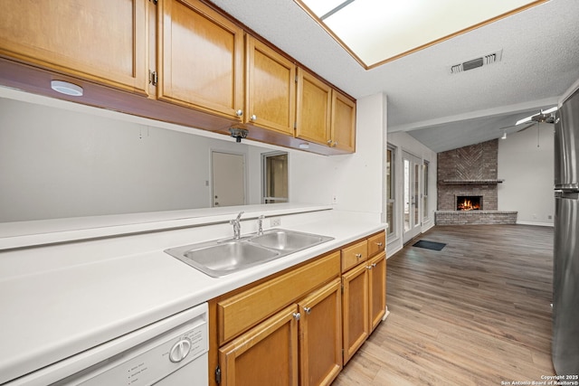 kitchen with a fireplace, lofted ceiling, sink, white dishwasher, and light hardwood / wood-style flooring