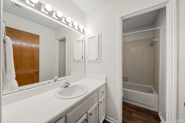 bathroom with hardwood / wood-style flooring, vanity, tiled shower / bath combo, and a textured ceiling