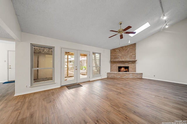 unfurnished living room with wood-type flooring, a skylight, a brick fireplace, a textured ceiling, and ceiling fan