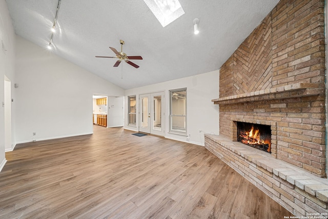 unfurnished living room with a brick fireplace, a textured ceiling, wood-type flooring, and a skylight