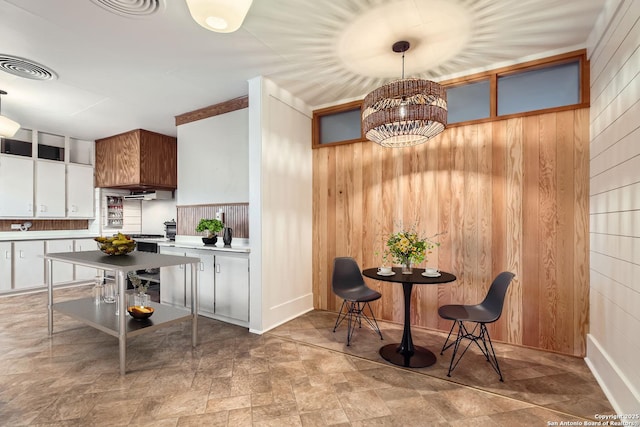 kitchen featuring white cabinetry, pendant lighting, and wood walls