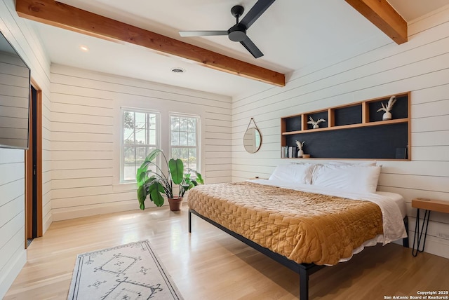 bedroom featuring beam ceiling, light hardwood / wood-style flooring, ceiling fan, and wood walls