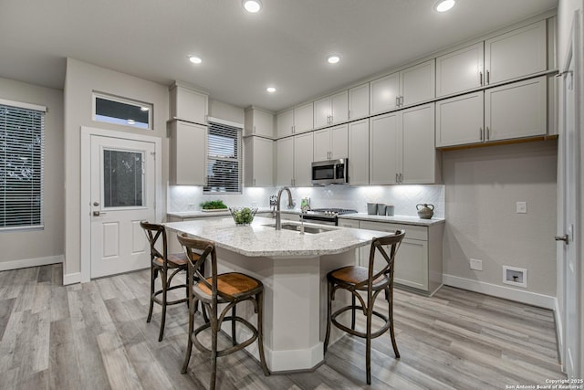 kitchen with a breakfast bar, tasteful backsplash, an island with sink, sink, and light stone countertops