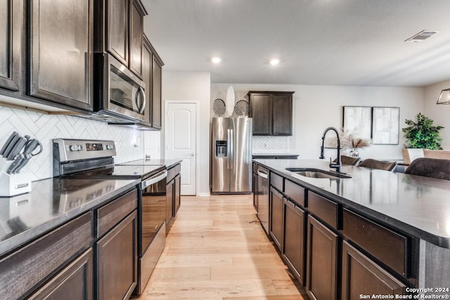 kitchen with sink, appliances with stainless steel finishes, dark brown cabinets, light hardwood / wood-style floors, and a center island with sink