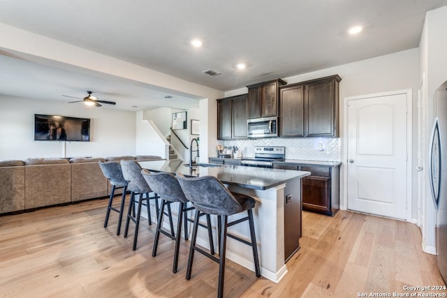 kitchen featuring sink, a breakfast bar area, dark brown cabinets, stainless steel appliances, and an island with sink